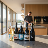 Five wine bottles from the brand 'Soleil' lined up on a modern kitchen island, with a man blurred in the background preparing food in a bright kitchen.