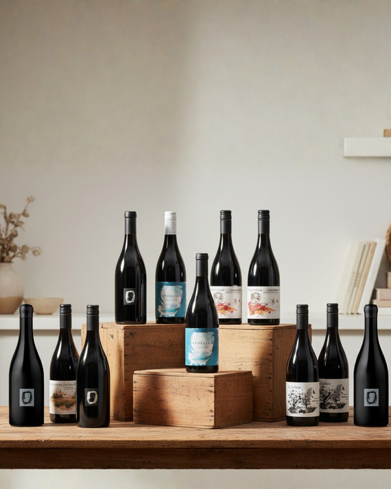 A group of wine bottles arranged on a plain white background, including several dark bottles with labels and a few lighter bottles with blue, white, and scenic illustrations on the labels.